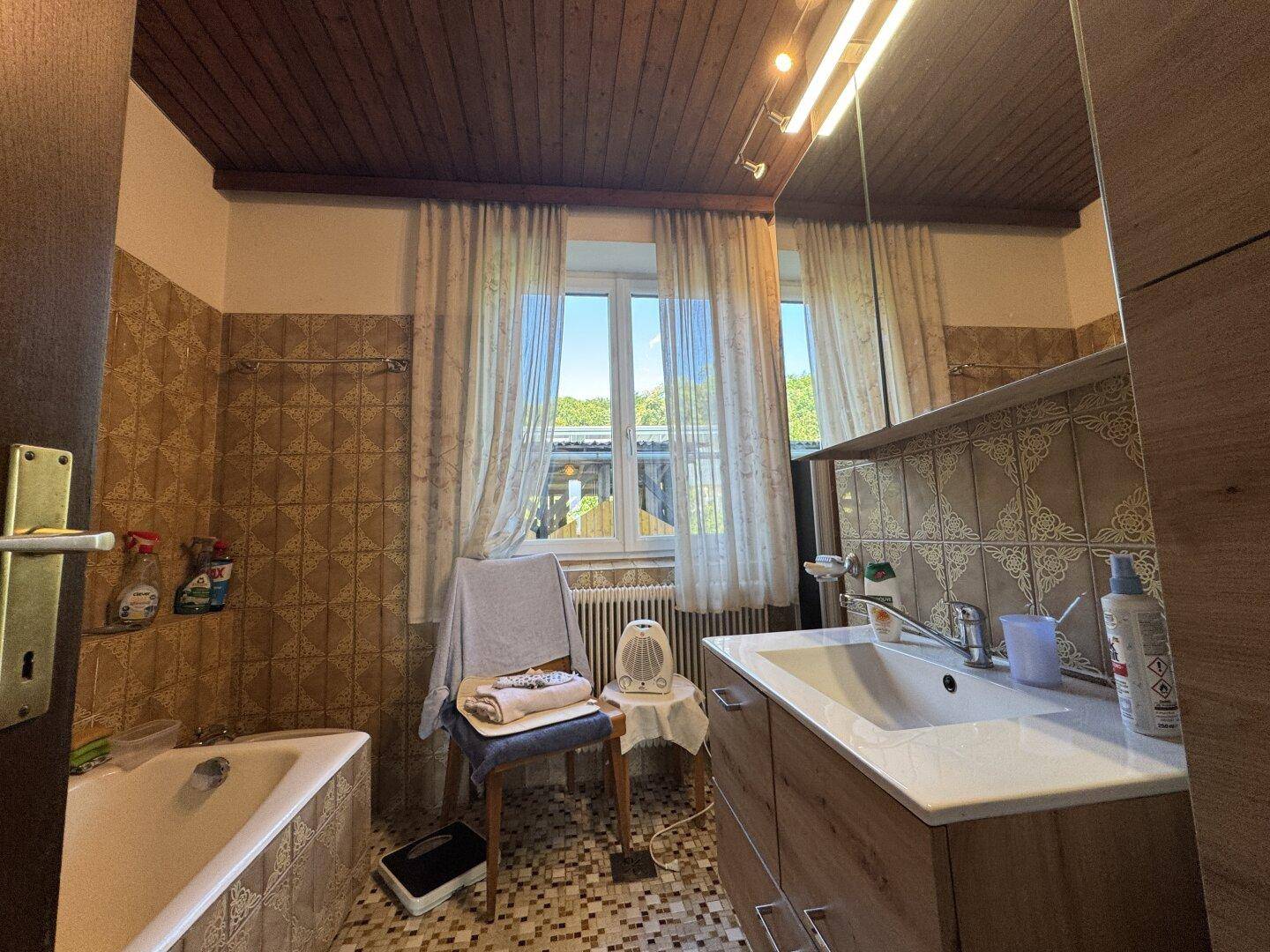 Badezimmer mit braunen Fliesen, Holzdecke, Badewanne und Fenster.