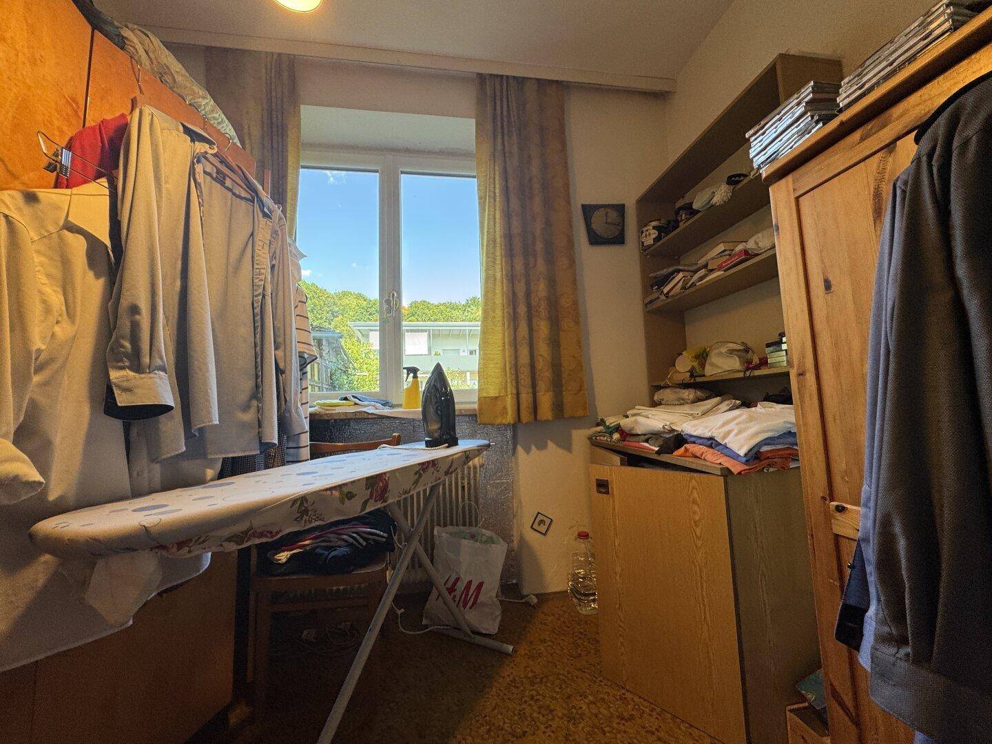 Abstellraum oder Waschküche mit Fenster, Bügelbrett und Kleiderschrank.