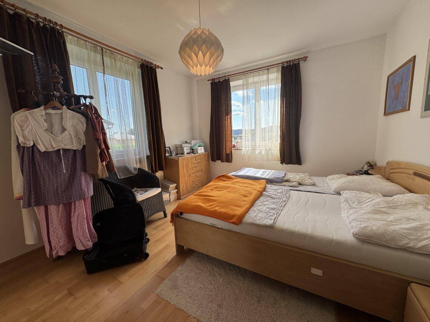 Schlafzimmer mit Doppelbett, Holzmöbeln, Teppich und zwei Fenstern.