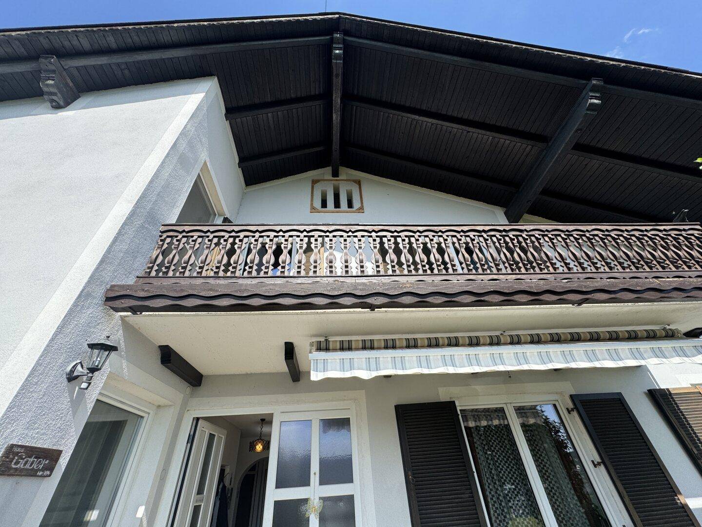 Traditioneller Holzbalkon mit aufwendigem Geländer und Markise an der Hausfassade.