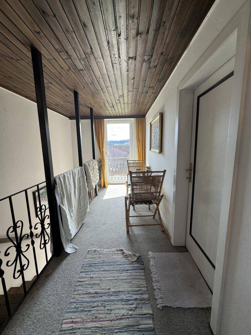 Heller Flur im Obergeschoss mit Holzdecke, Teppichboden und Zugang zu einem Balkon.