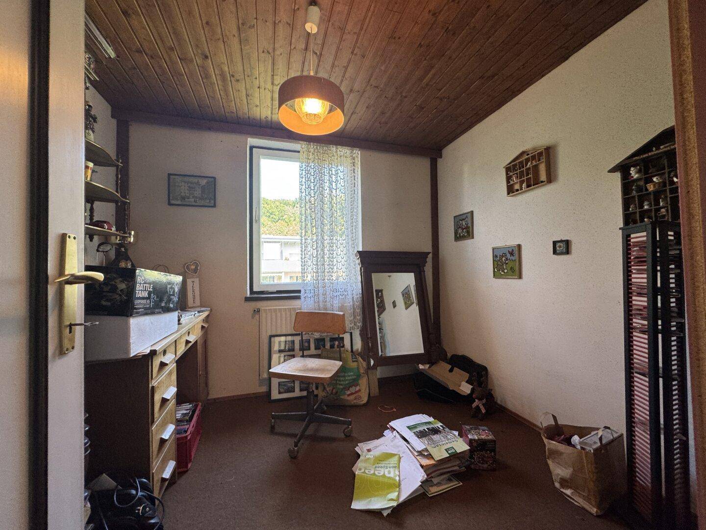 Zimmer mit Holzdecke, Teppichboden, Schreibtisch und Fenster mit Ausblick.