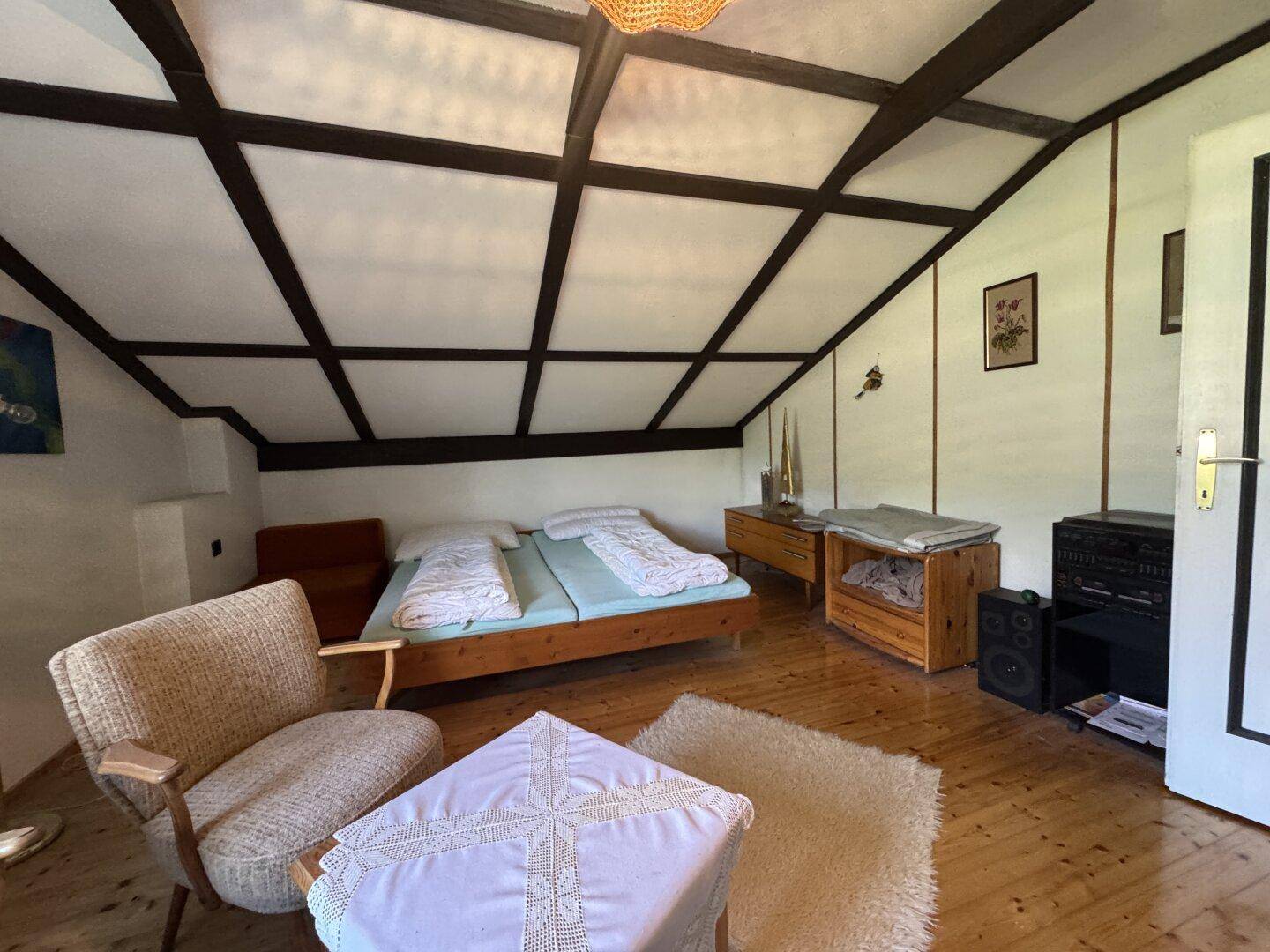 Schlafzimmer im Dachgeschoss mit Holzbalkendecke, Doppelbett und rustikalen Möbeln.