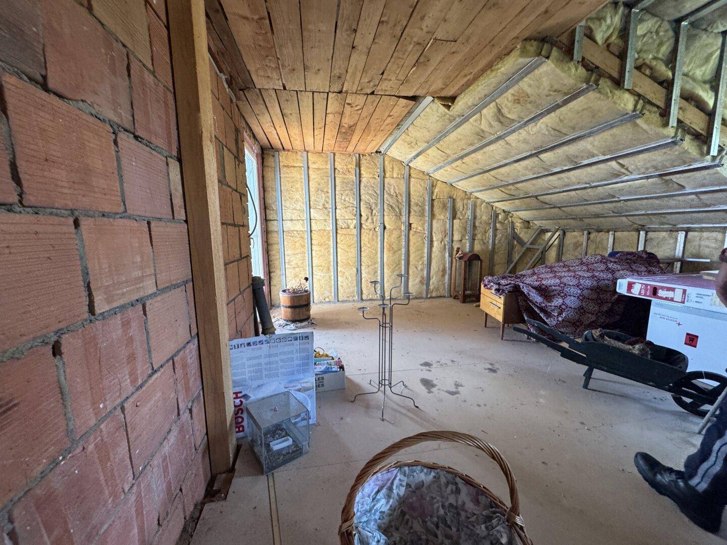 Unausgebauter Dachboden mit Ziegelwänden, Holzdecke und Isolierung.