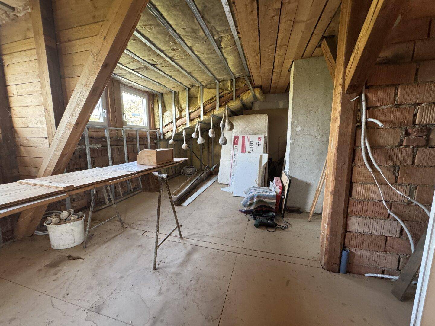Unausgebauter Dachboden mit sichtbaren Holzbalken und Ziegelwänden, bereit für den Ausbau.