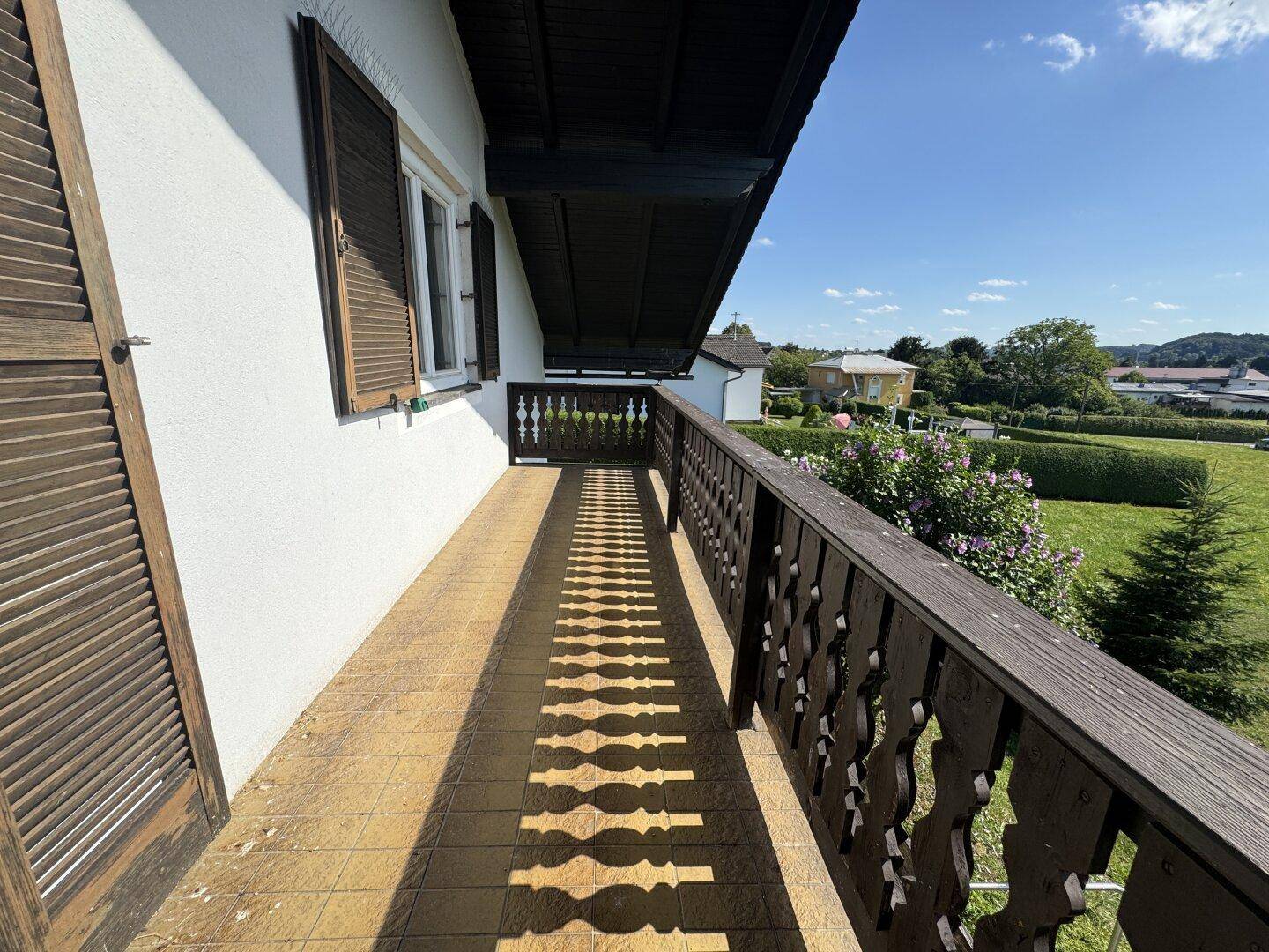 Traditioneller Balkon mit Holzbalkongeländer und Fliesenboden, bietet einen weiten Blick ins Grüne.