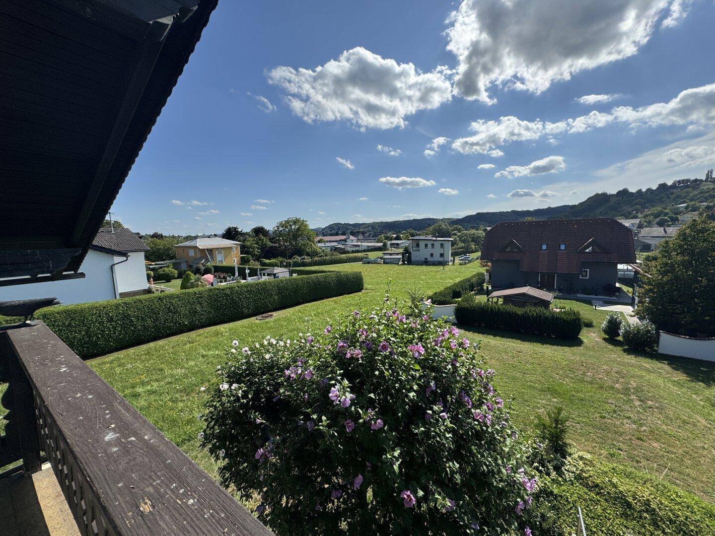 Weitläufiger Blick vom Balkon über grüne Wiesen, Hecken und die umliegende Landschaft.