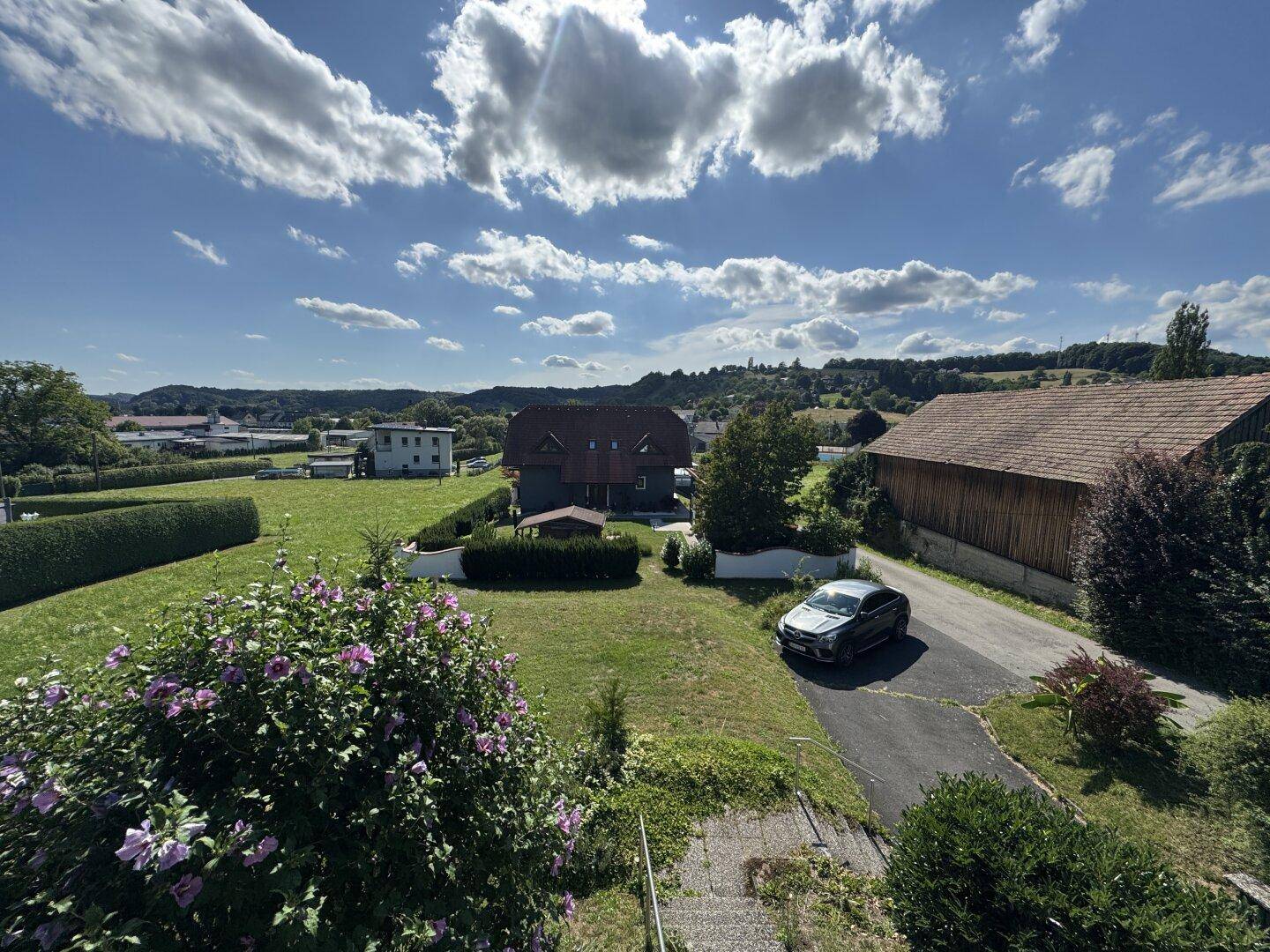Panoramablick vom Balkon auf die Zufahrt, ein Auto und die idyllische ländliche Umgebung.