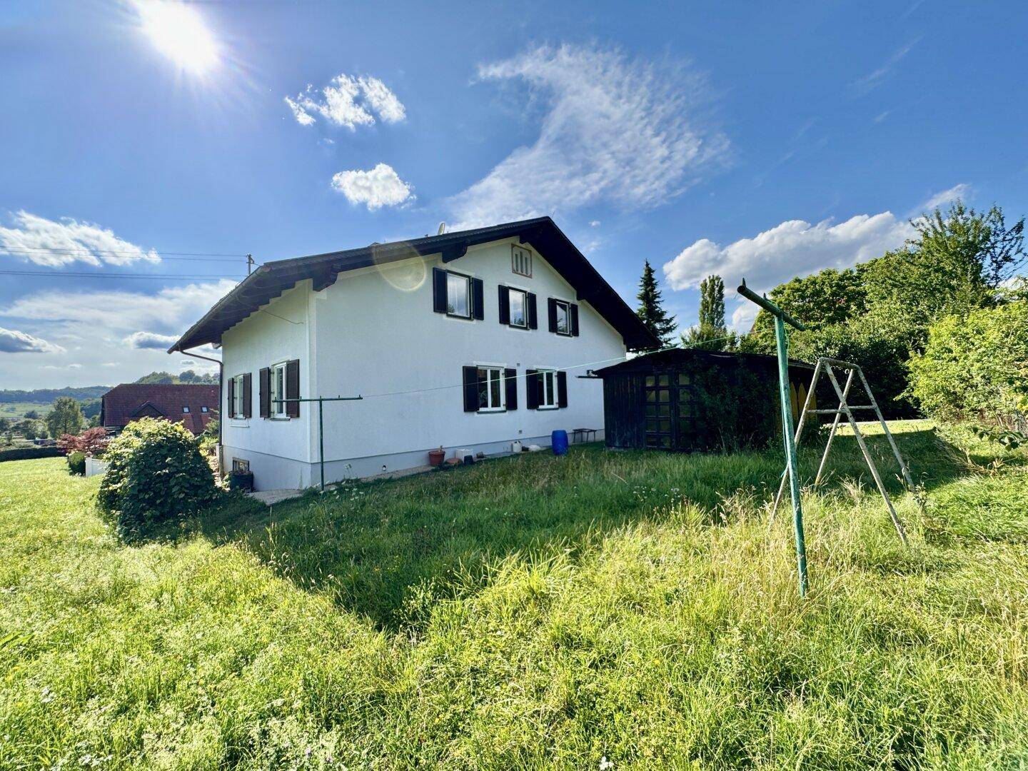 Seitenansicht des Hauses mit weißer Fassade und großem Gartenbereich mit Schaukel.