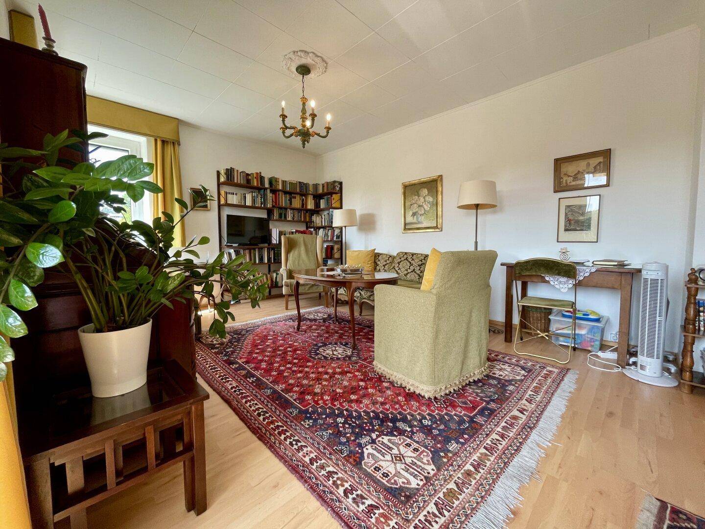 Helles Wohnzimmer mit traditionellem Interieur, Bücherregal und großem Orientteppich.