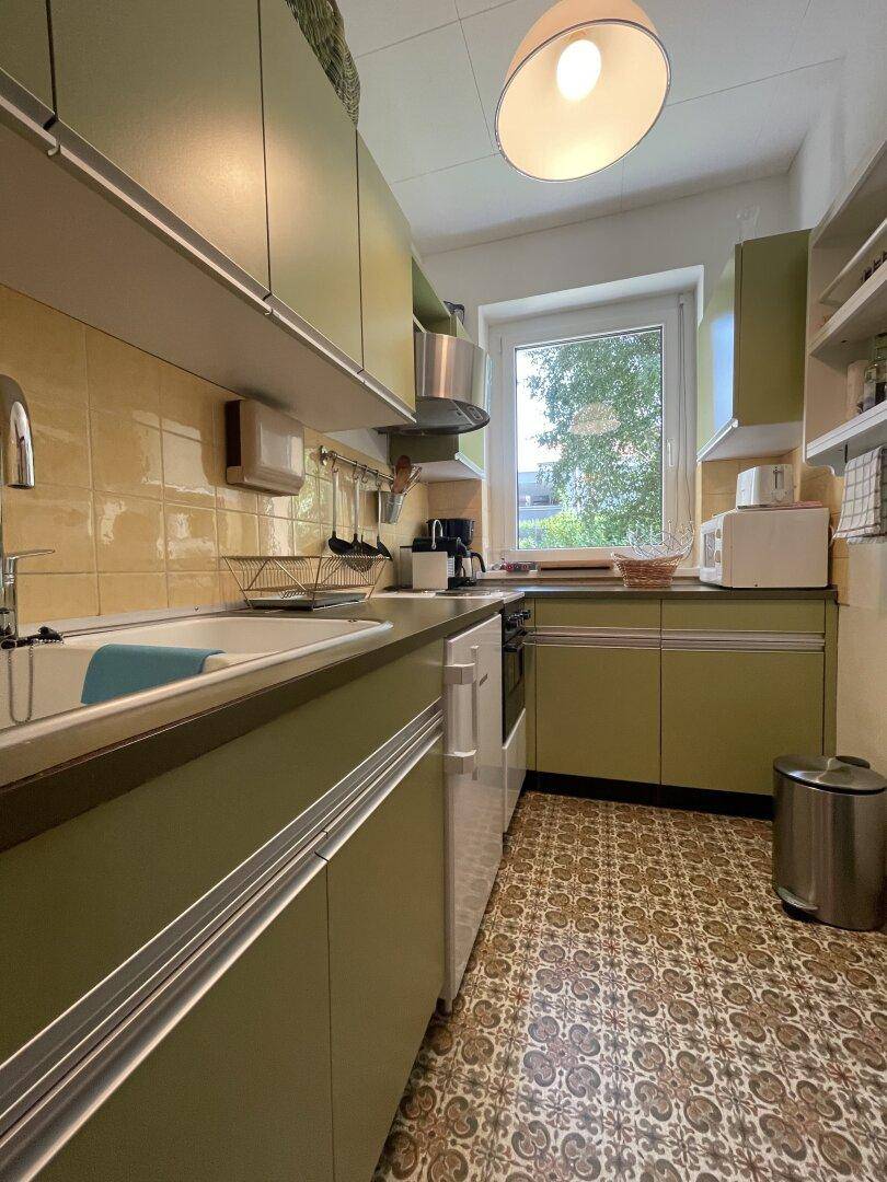 Küche im Retro-Stil mit grünen Schränken, gelben Fliesen und gemustertem Boden.