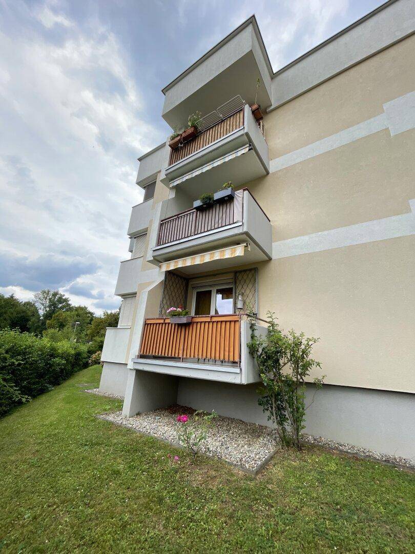Mehrstöckiges Wohngebäude mit Balkonen und gepflegter Grünfläche.