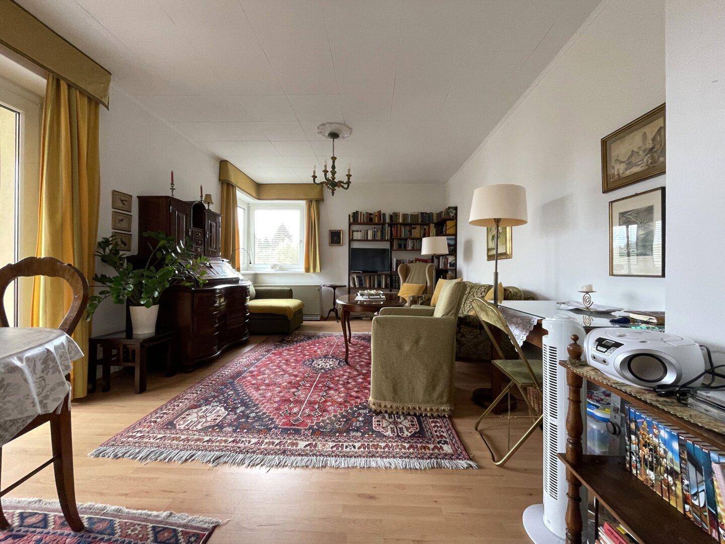 Geräumiges Wohnzimmer mit traditionellen Möbeln, Teppich und Zugang zum Balkon.