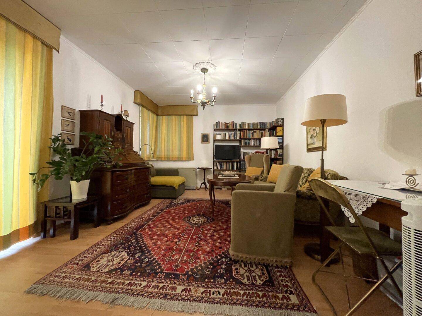 Geräumiges Wohnzimmer mit traditionellen Möbeln, Teppich und Zugang zum Balkon.