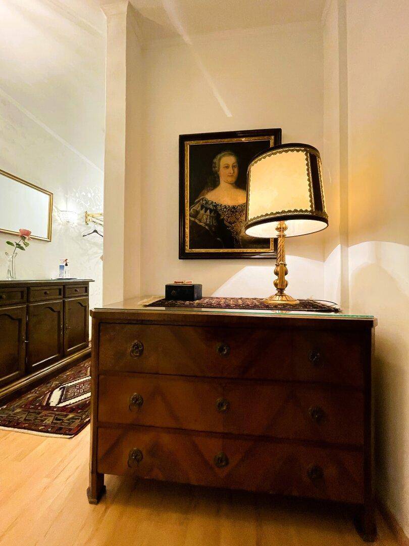 Eingangsbereich mit antiker Kommode, Lampe und einem Gemälde an der Wand.