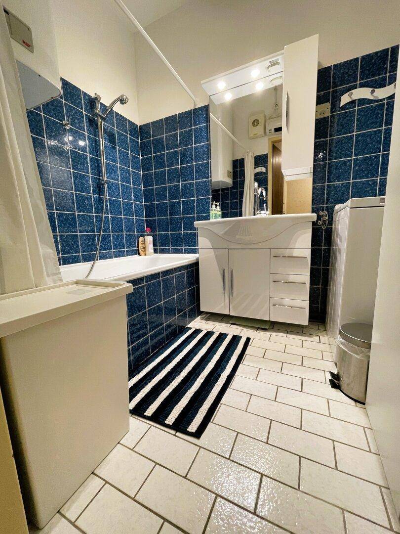 Badezimmer mit blauen Fliesen, Badewanne mit Duschfunktion und Waschbecken.