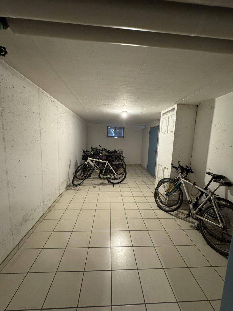 Fahrradraum im Keller mit Fliesenboden, Sichtbetonwänden und einem kleinen Fenster.