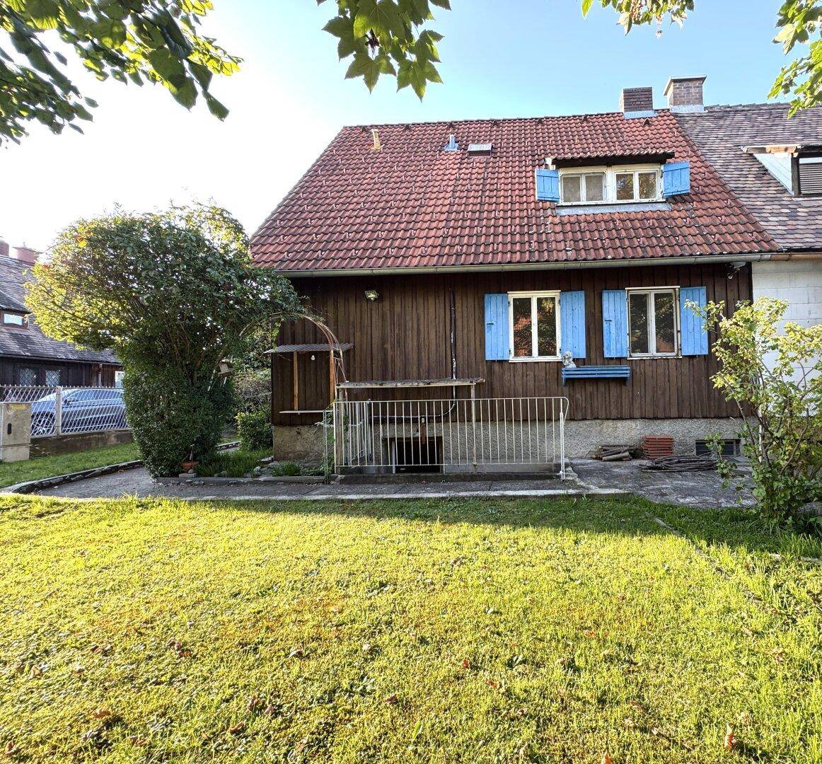 Rückansicht des Hauses mit Holzfassade, rotem Ziegeldach und grünem Rasen im Sonnenlicht.