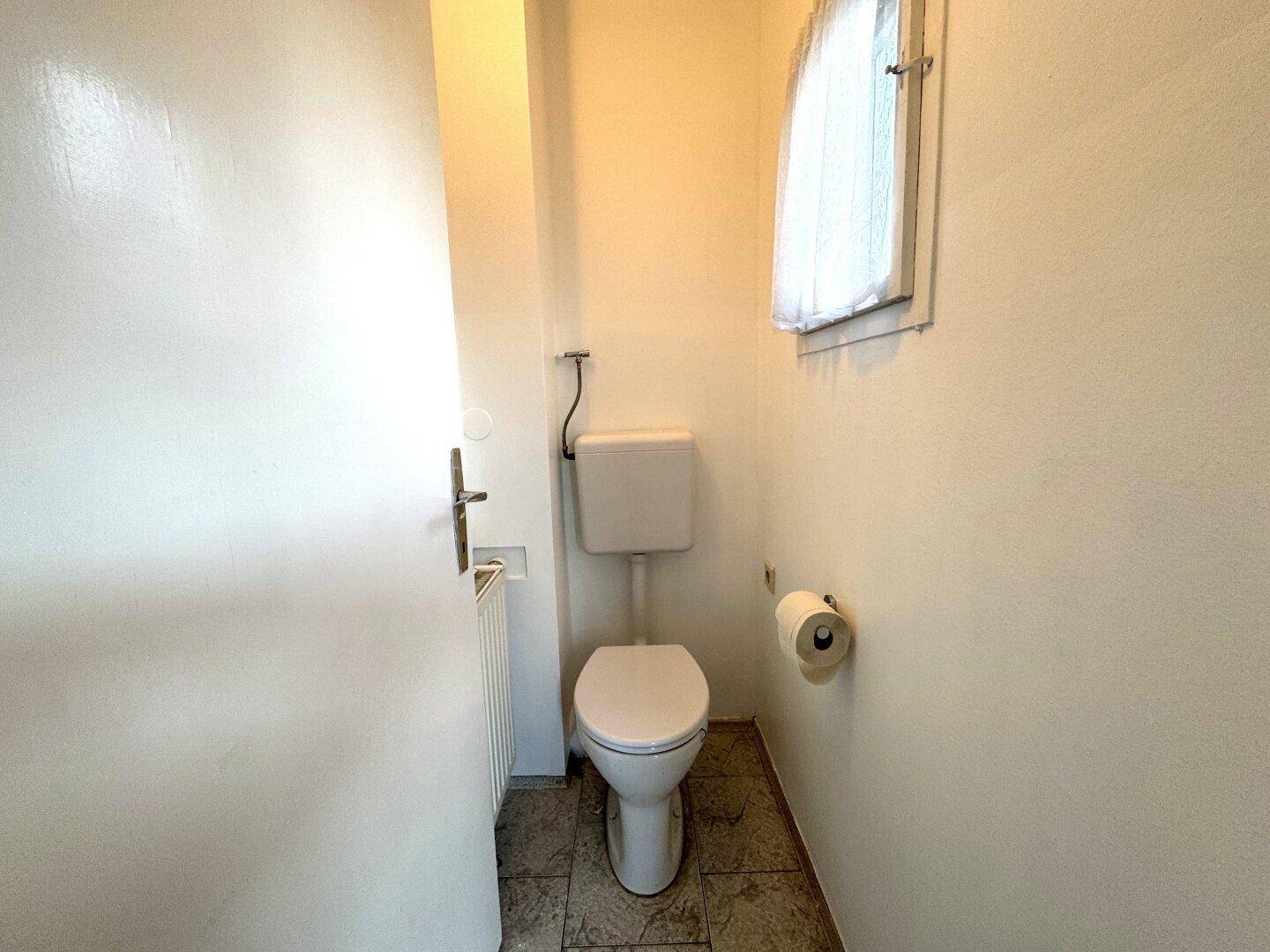 Kleines Gäste-WC mit Fenster, einfacher Toilette und Fliesenboden.