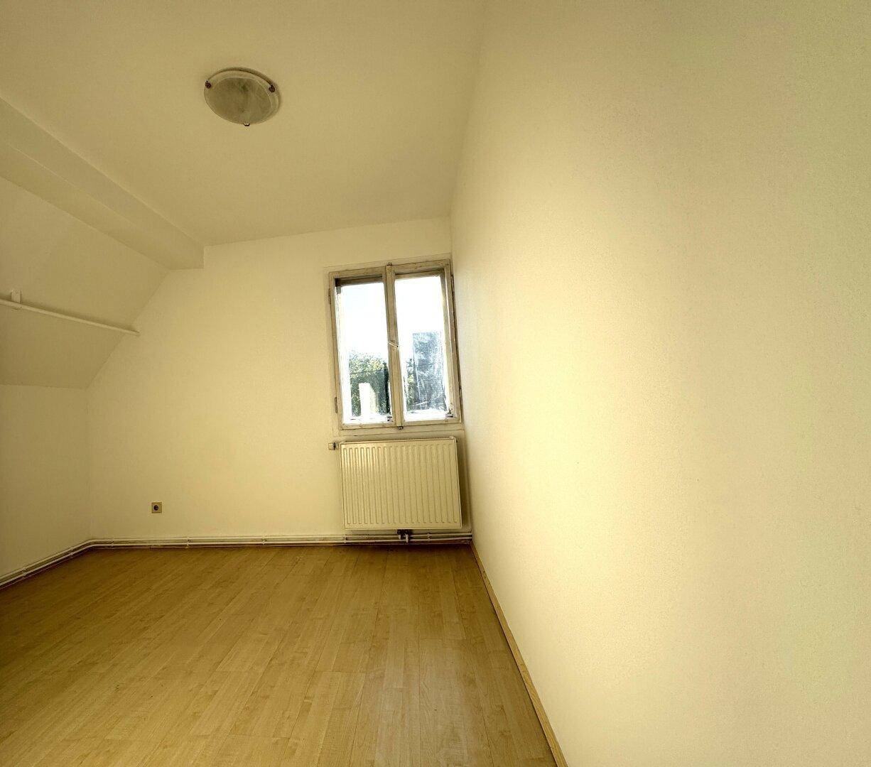 Helles Schlafzimmer im Dachgeschoss mit Laminatboden, weiß gestrichenen Wänden und Fenster.