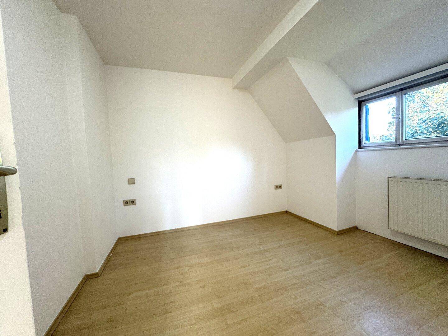 Helles Schlafzimmer im Dachgeschoss mit schrägen Wänden, Laminatboden und großem Fenster.
