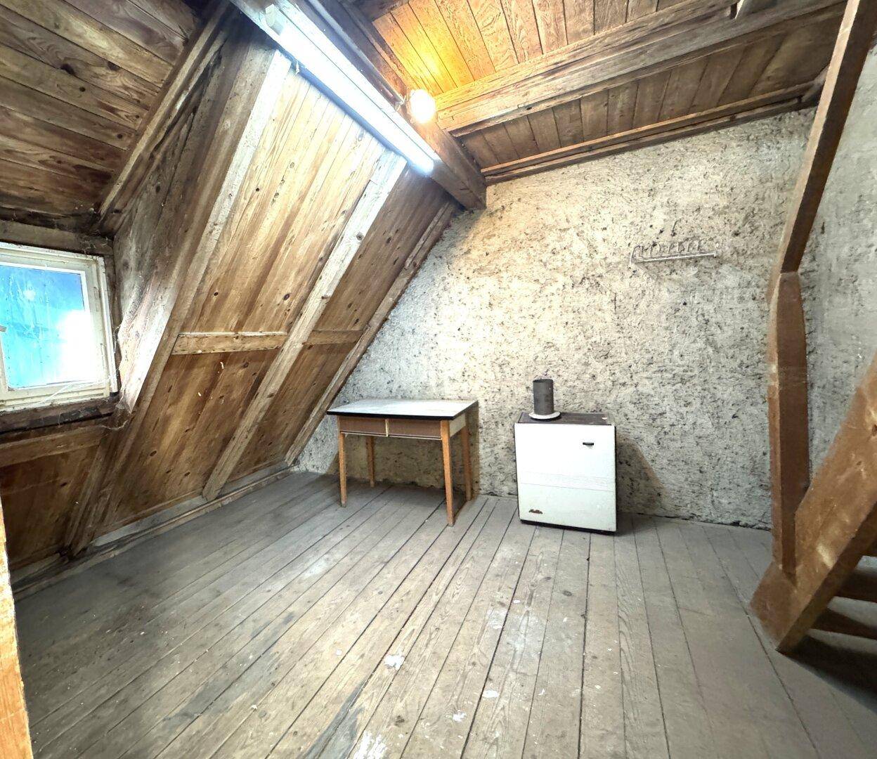 Rustikaler Dachboden mit Holzboden, sichtbaren Dachbalken und kleinem Fenster.