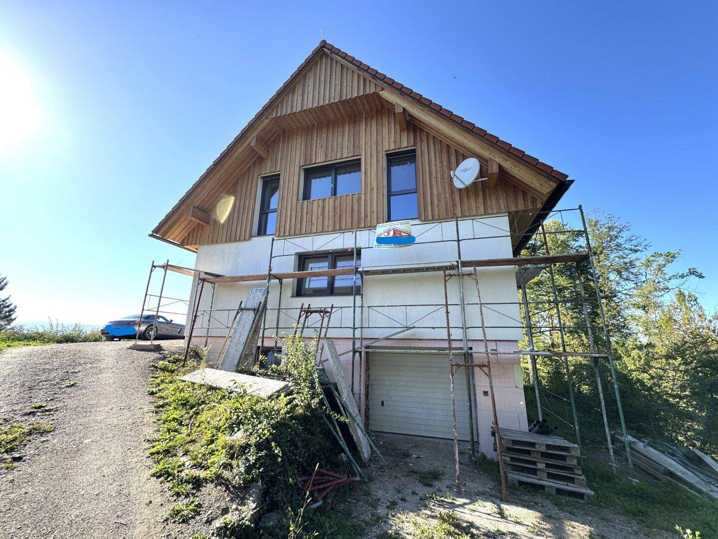Haus im Bau mit Holzfassade, Gerüst und einer Auffahrt.