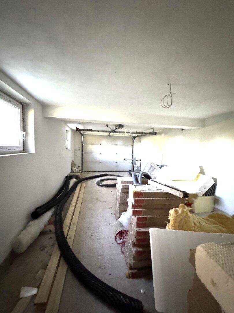 Garage im Rohbauzustand mit Baumaterialien und offenem Garagentor.