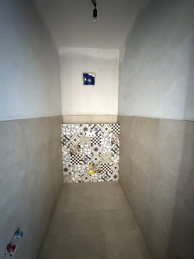 Kleiner Raum im Rohbau mit gemusterten Fliesen an der Wand.