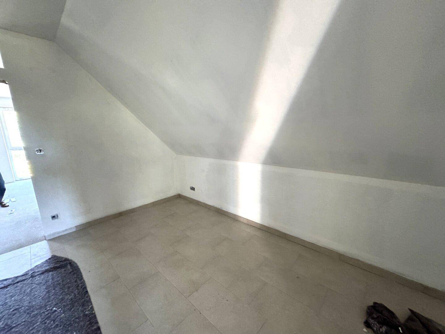 Raum mit schräger Decke und Fliesenboden, noch im Rohbauzustand.