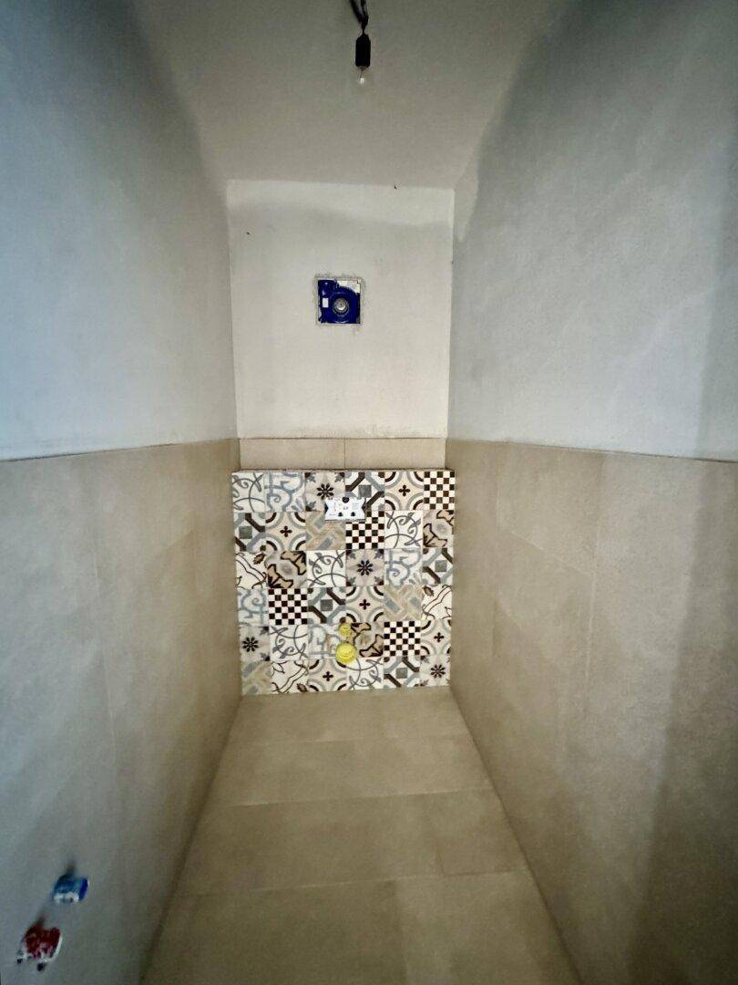 Kleiner Raum im Rohbau mit gemusterten Fliesen an der Wand.