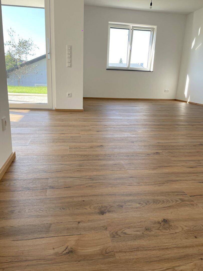 Lichtdurchfluteter Wohnbereich mit Laminatboden und Zugang zur Terrasse, bietet viel Tageslicht.