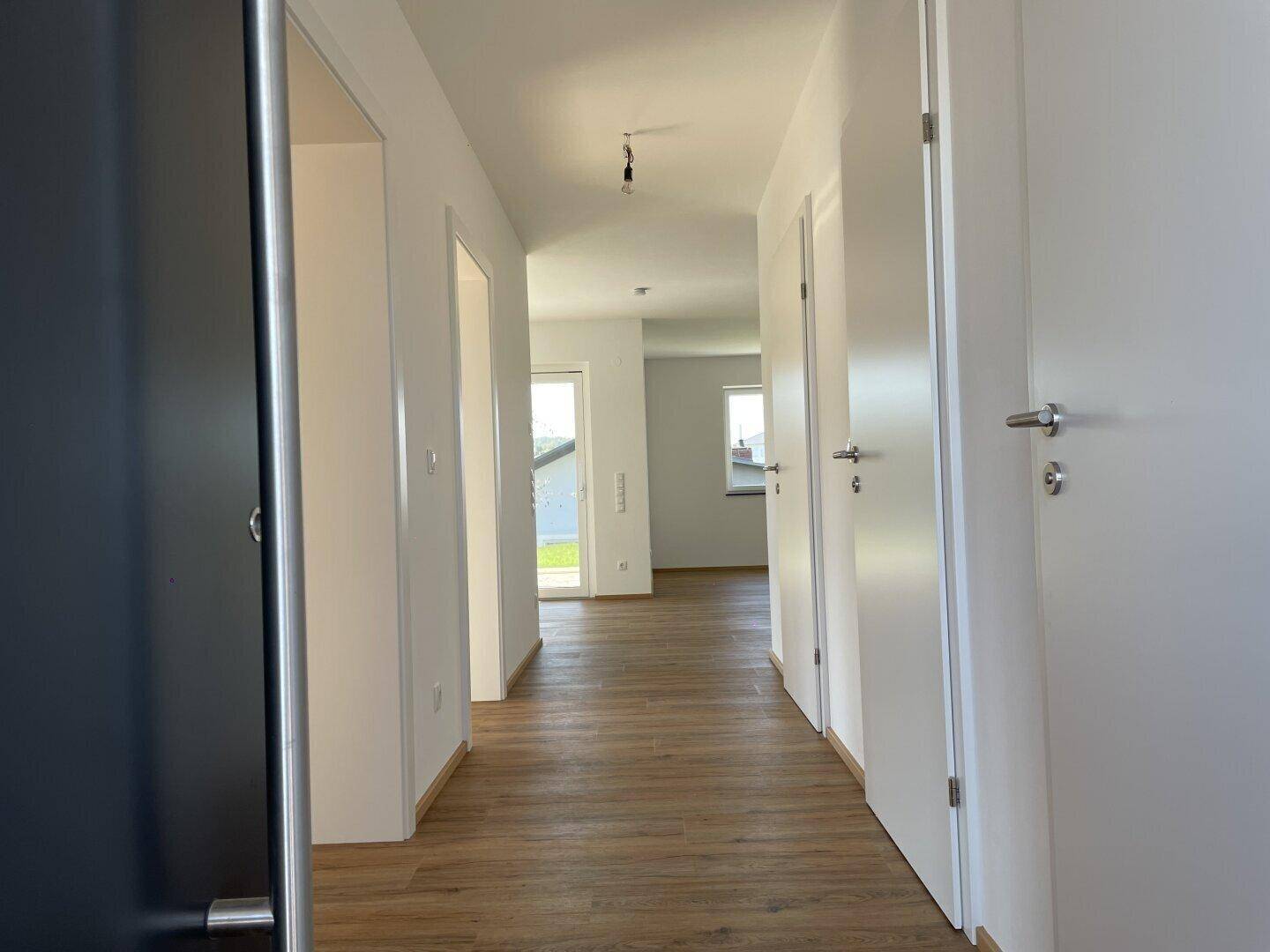 Heller Flur mit modernem Laminatboden und weißen Türen, der zu weiteren Räumen führt.