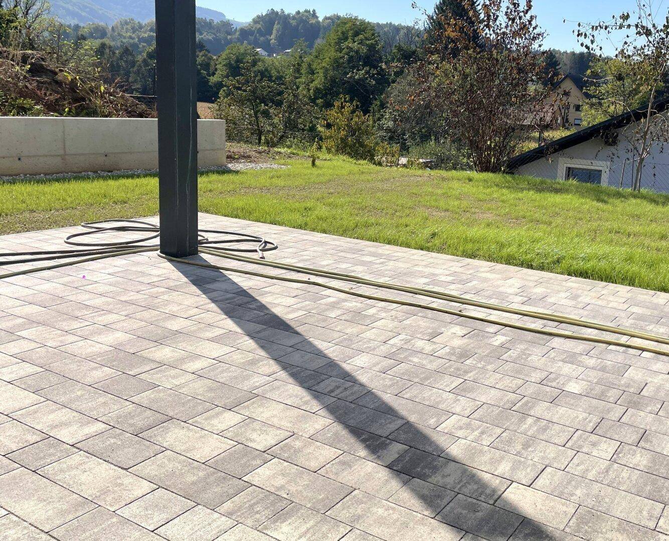 Gepflasterte Terrasse mit Rasenfläche und Blick ins Grüne, ideal für entspannte Stunden im Freien.