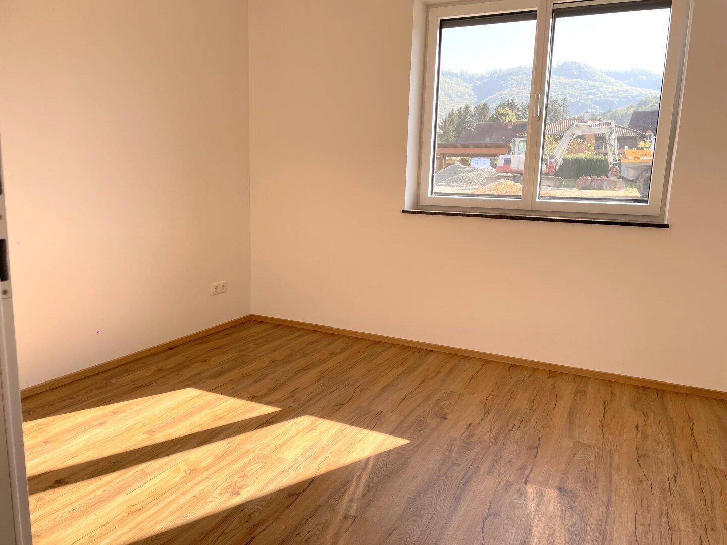 Schlafzimmer mit Laminatboden und großem Fenster, das einen Blick auf die grüne Umgebung bietet.
