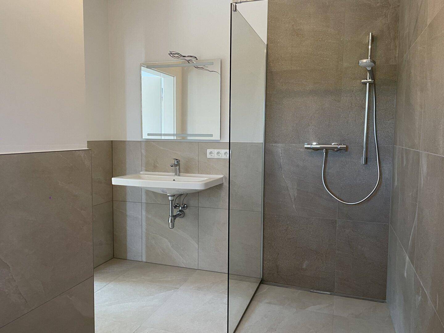 Badezimmer mit begehbarer Dusche, Waschbecken und Spiegel, ausgestattet mit modernen Armaturen.