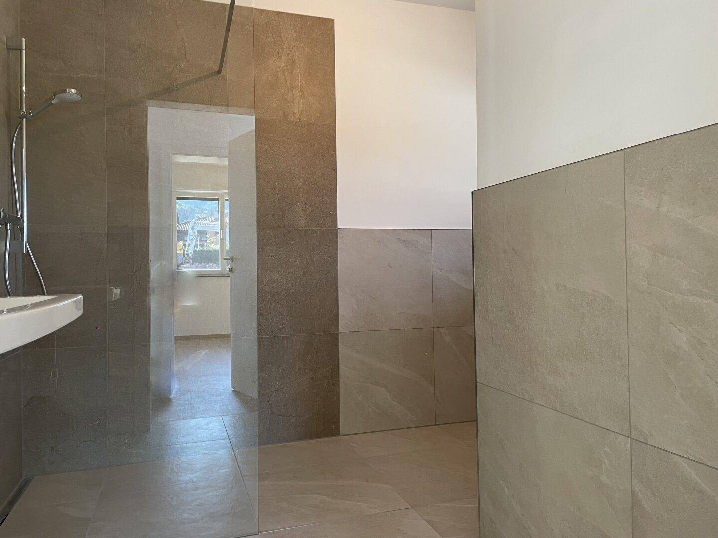 Modernes Badezimmer mit begehbarer Dusche und großformatigen Fliesen in warmen Erdtönen.
