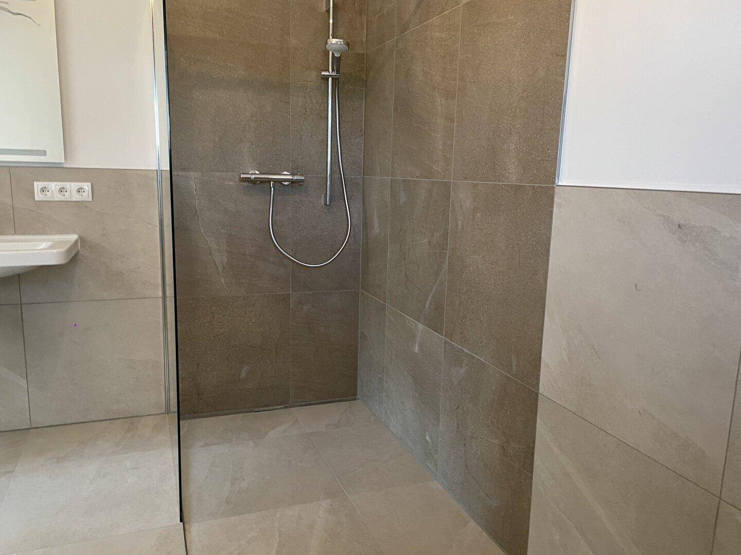 Geräumige begehbare Dusche mit modernen Fliesen und Duscharmatur in einem hellen Badezimmer.