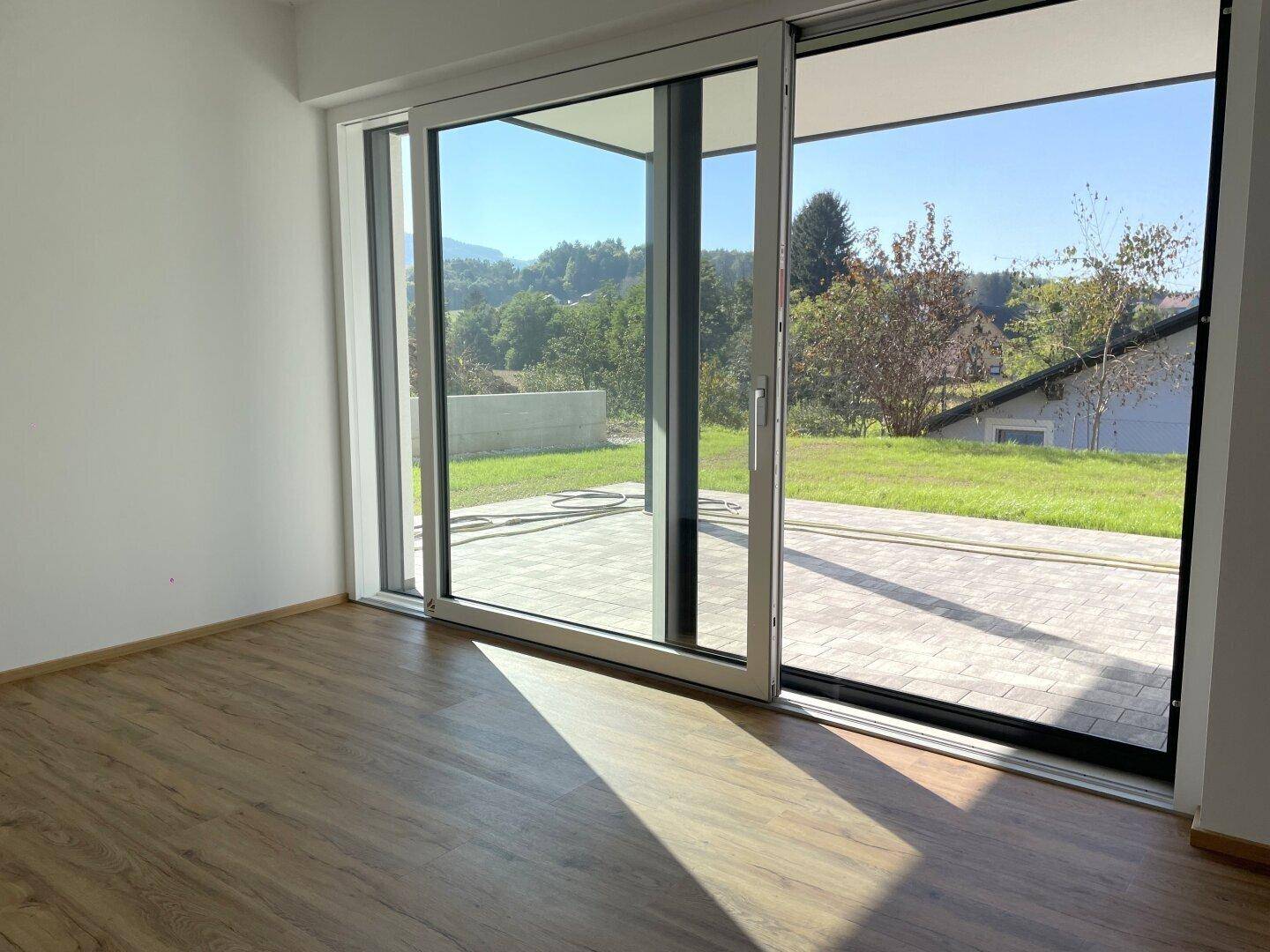 Wohnbereich mit großen Schiebetüren zur Terrasse und Blick ins Grüne, sehr hell und offen.