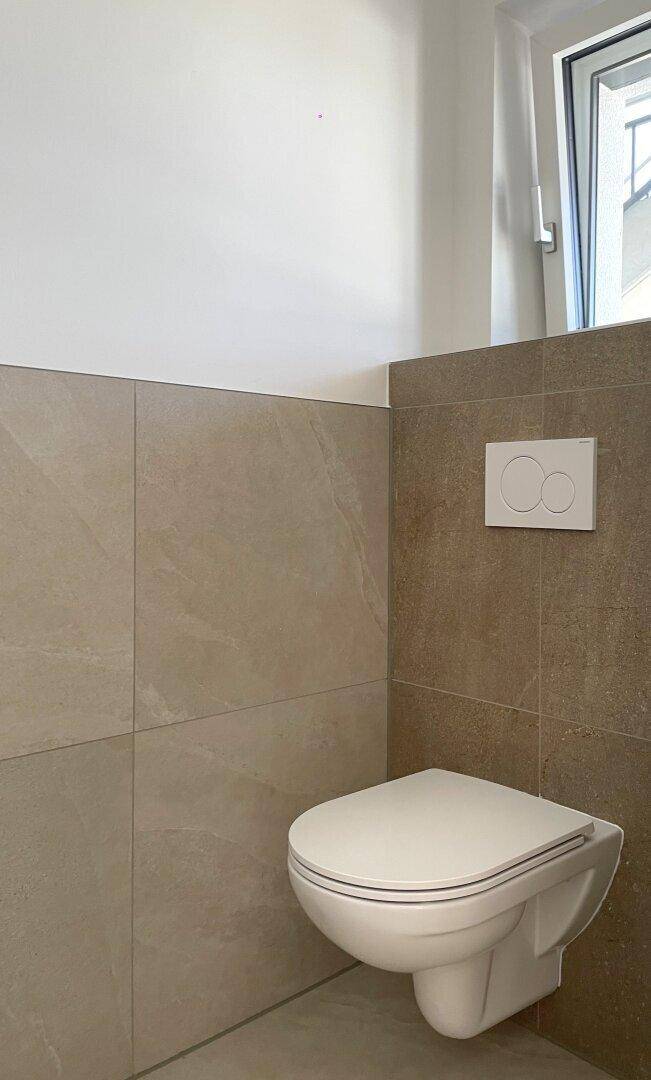 Wandhängendes WC in einem hell gefliesten Raum mit Fenster, sauber und modern gestaltet.