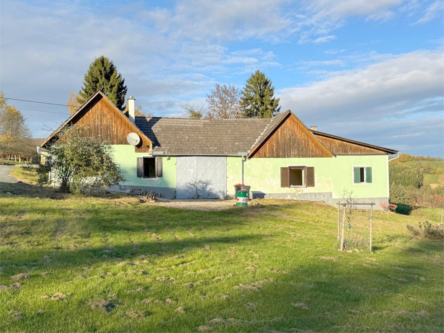 Ansicht des ländlichen Hauses mit grüner Fassade, Holzelementen und Satteldach, umgeben von Rasen.