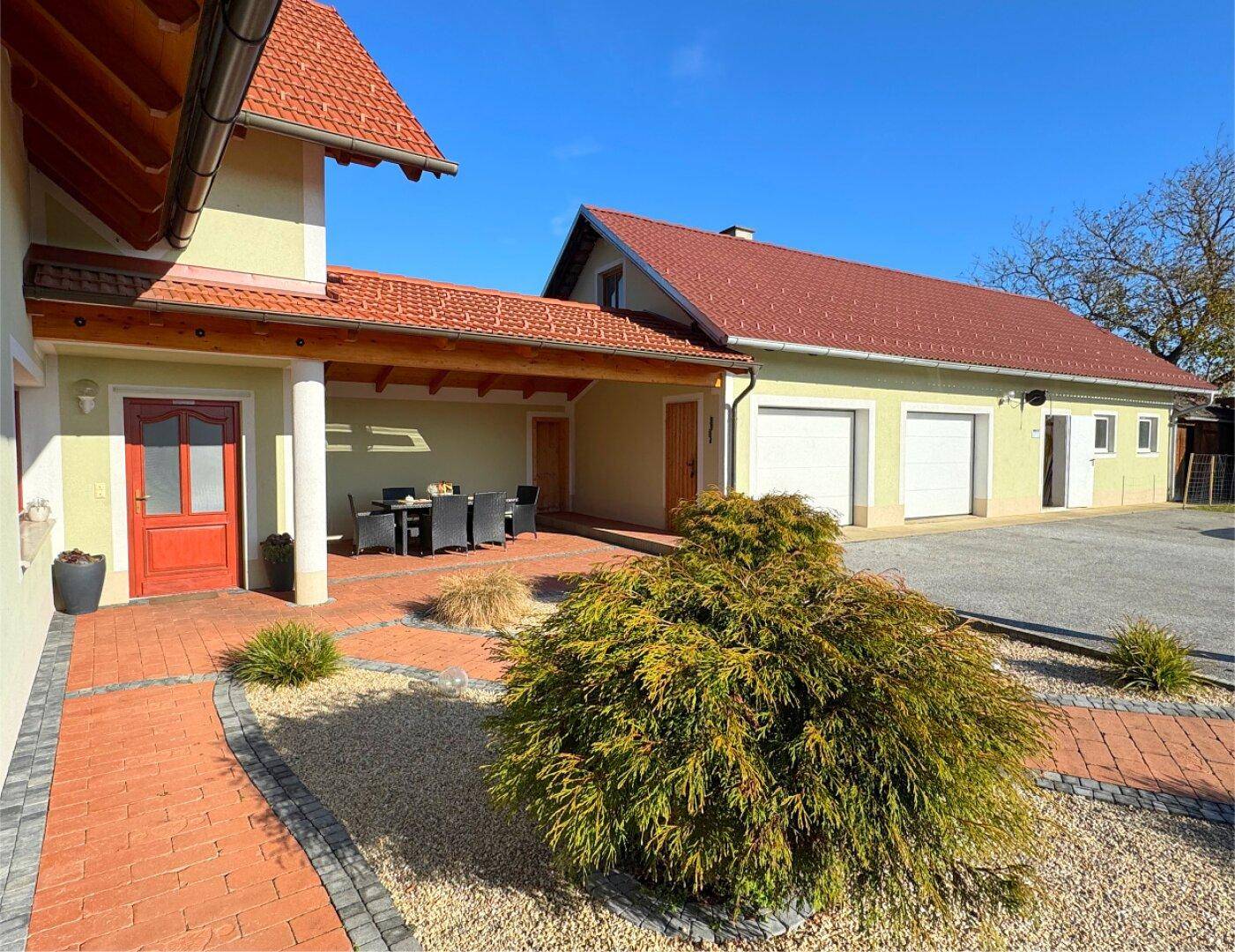 Eingangsbereich mit überdachter Terrasse, Sitzgelegenheiten und einem gepflasterten Gartenweg.