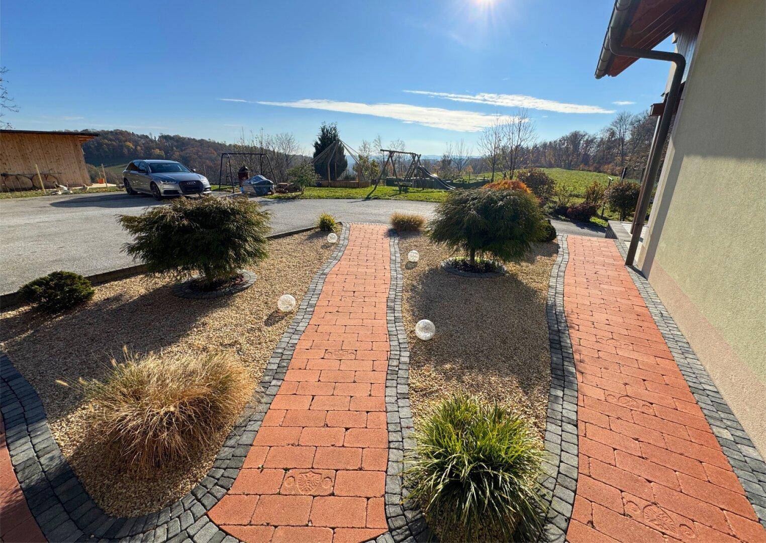 Gepflegter Gartenweg mit dekorativen Leuchten und Blick auf die umliegende Landschaft.