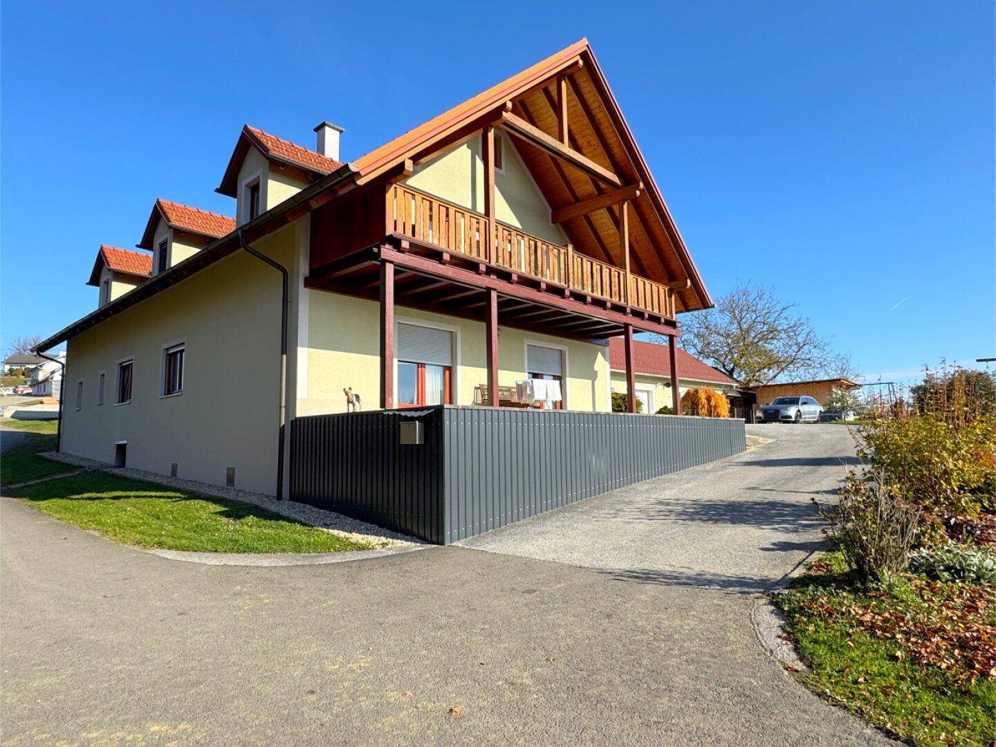 Seitenansicht des Hauses mit einem langen Holzbalkon und der Zufahrt zum Grundstück.