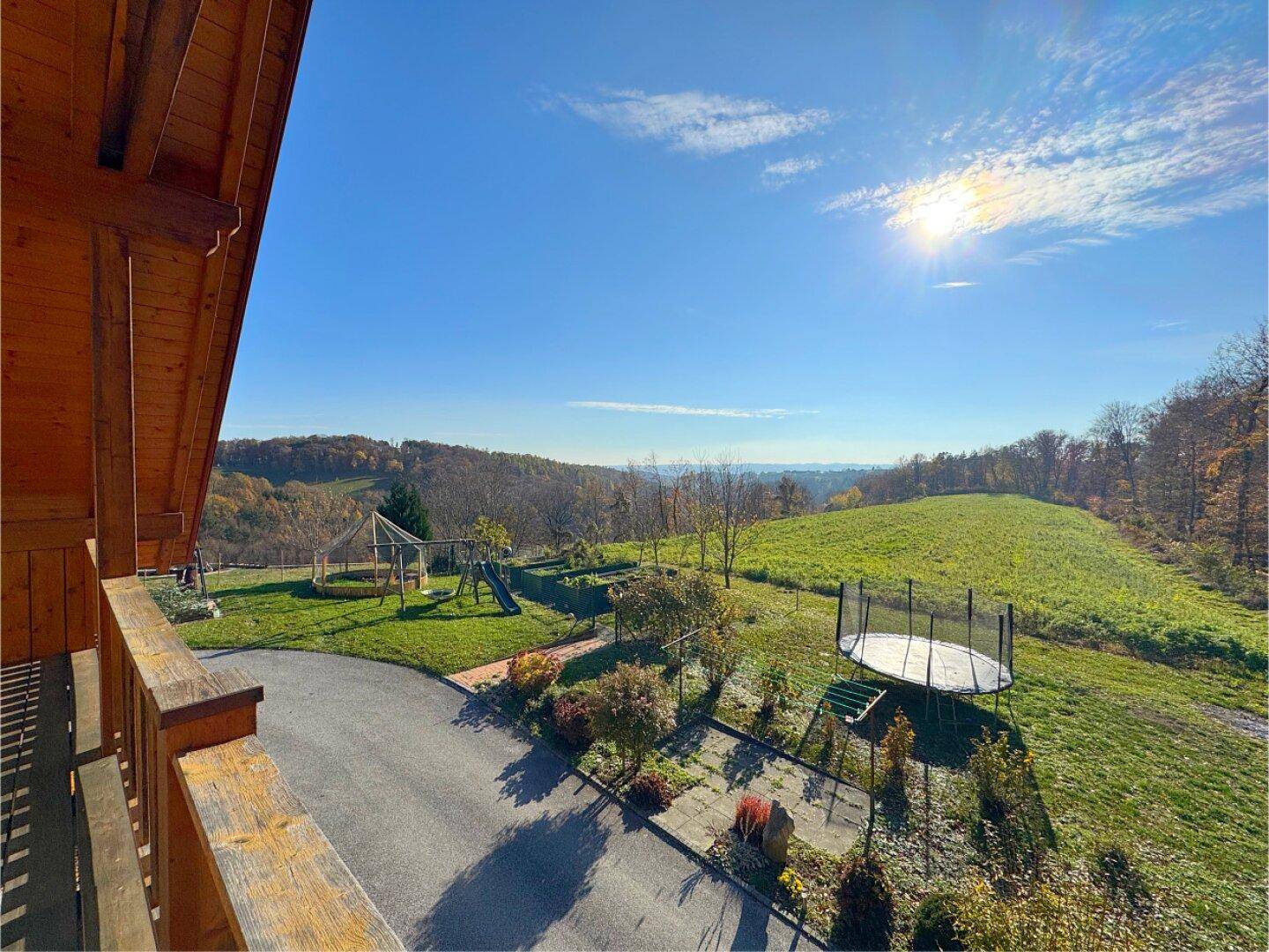 Panoramablick vom Balkon auf den Garten mit Spielplatz und die weite, grüne Landschaft.