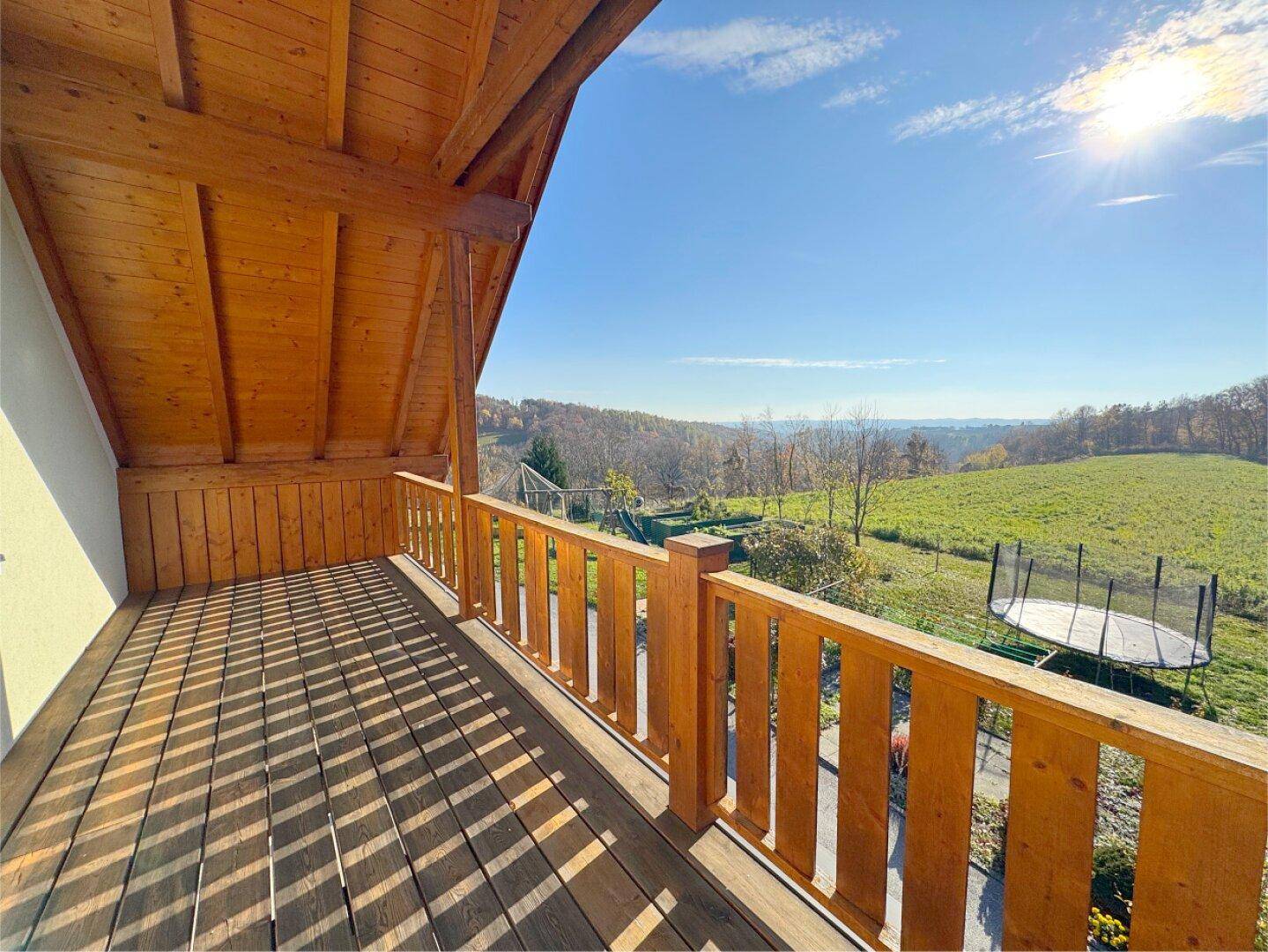 Geräumiger Holzbalkon mit Blick auf die hügelige Landschaft unter strahlend blauem Himmel.