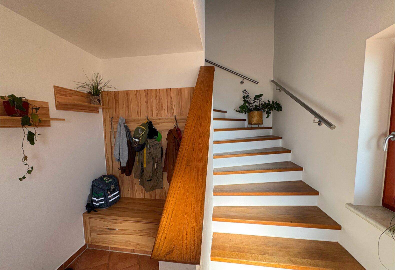 Heller Eingangsbereich mit Holztreppe und einer praktischen Garderobe aus Holz.