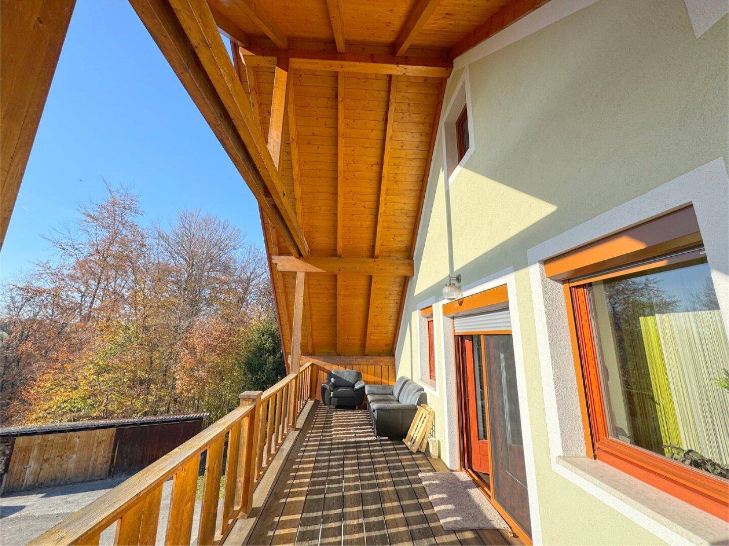 Langer Holzbalkon mit bequemen Sitzgelegenheiten und einem schönen Ausblick ins Grüne.