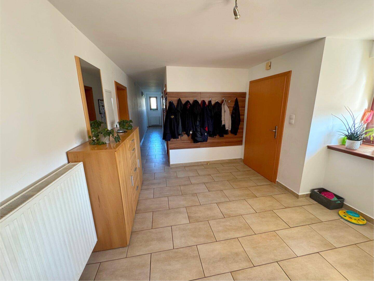 Geräumiger Flur mit Fliesenboden, Heizkörper und einer Wandgarderobe für Jacken.