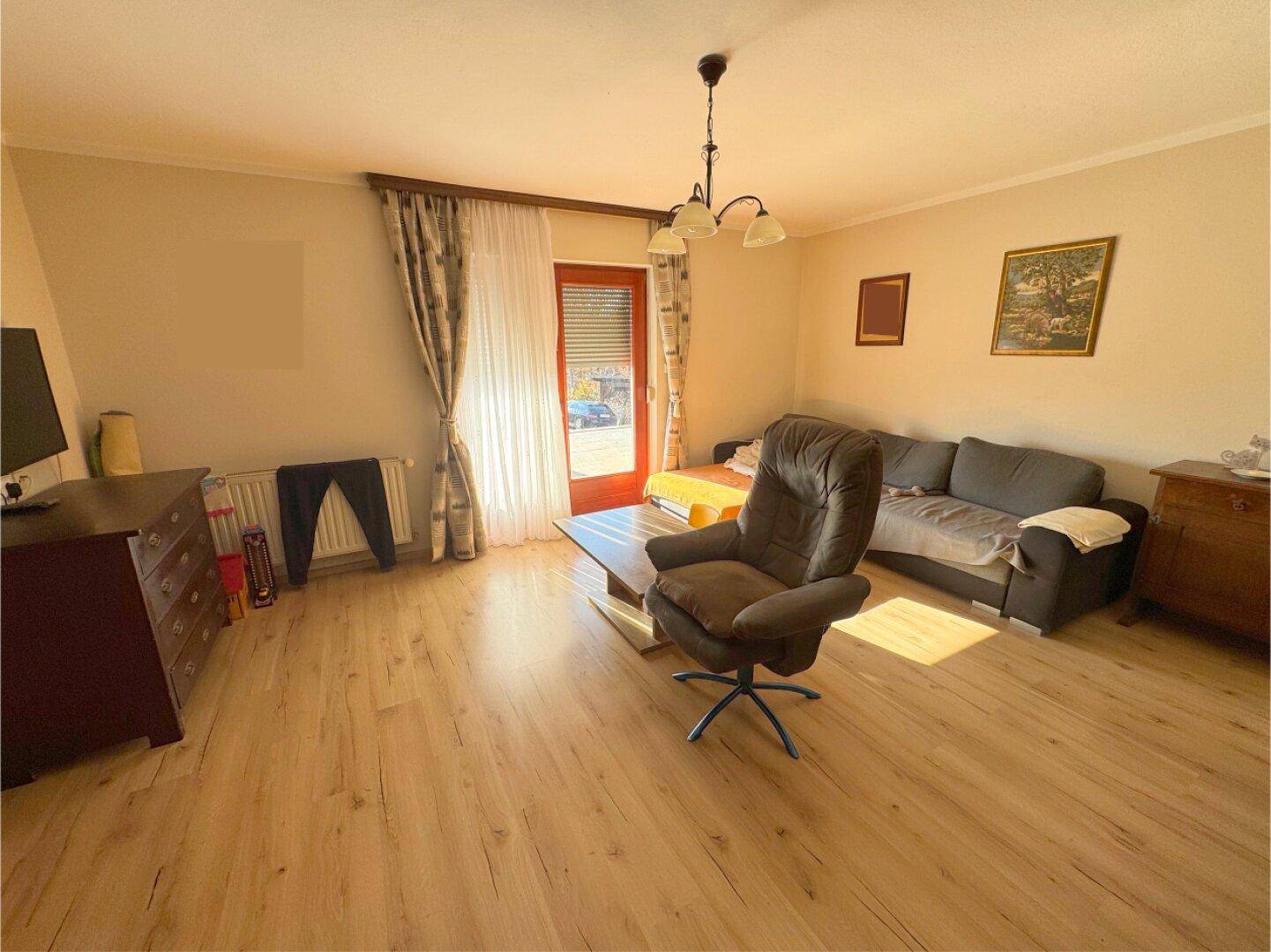 Helles Wohnzimmer mit Laminatboden, großem Fenster und Zugang zu einem Außenbereich.